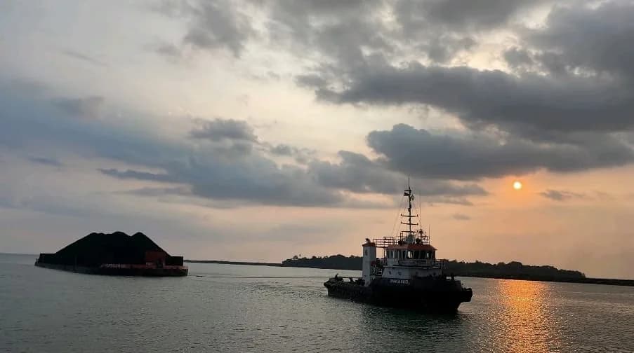Tug and loaded barge sailing during sunset